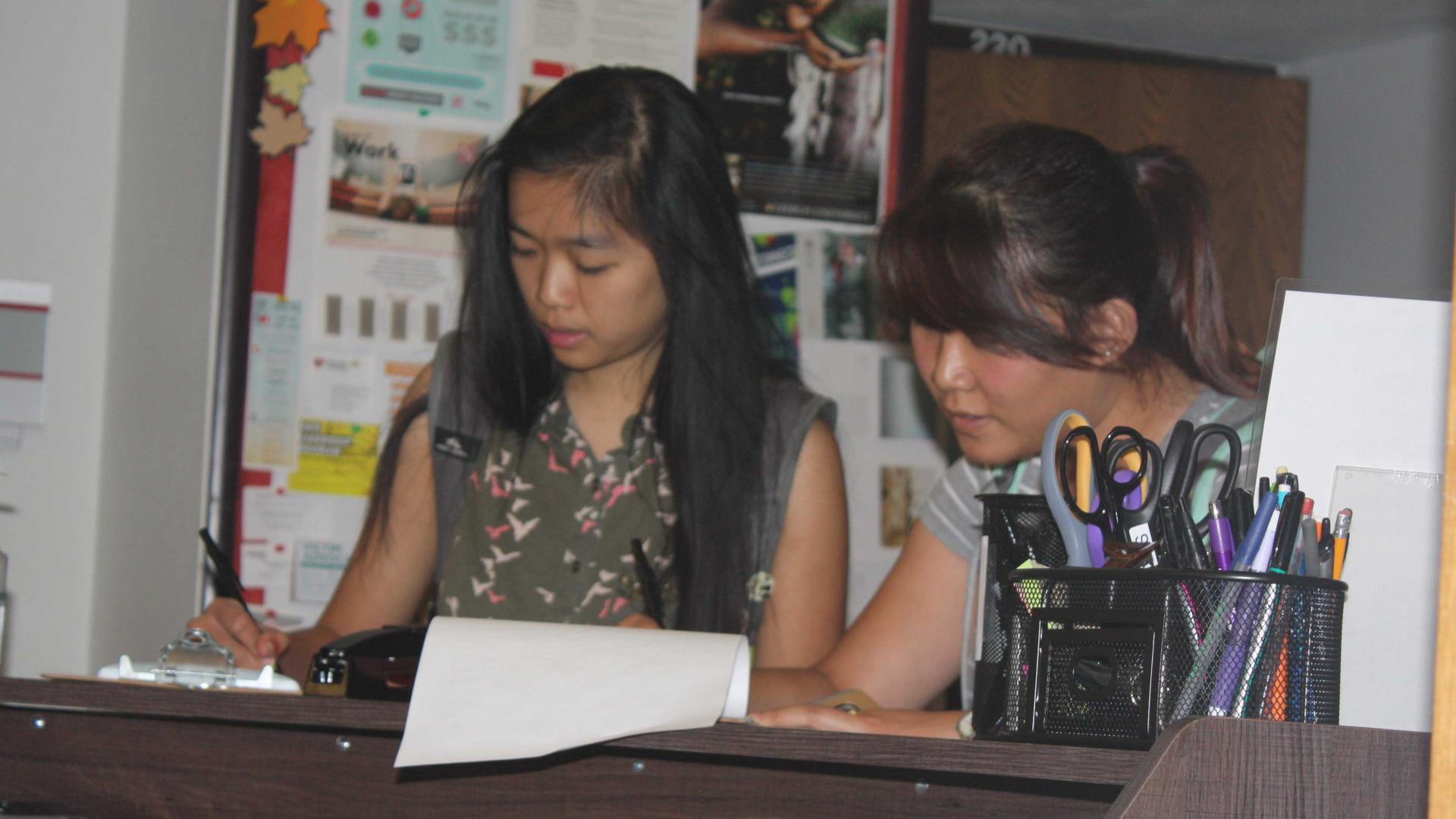 Two female students work the check in desk in the TRIO office.