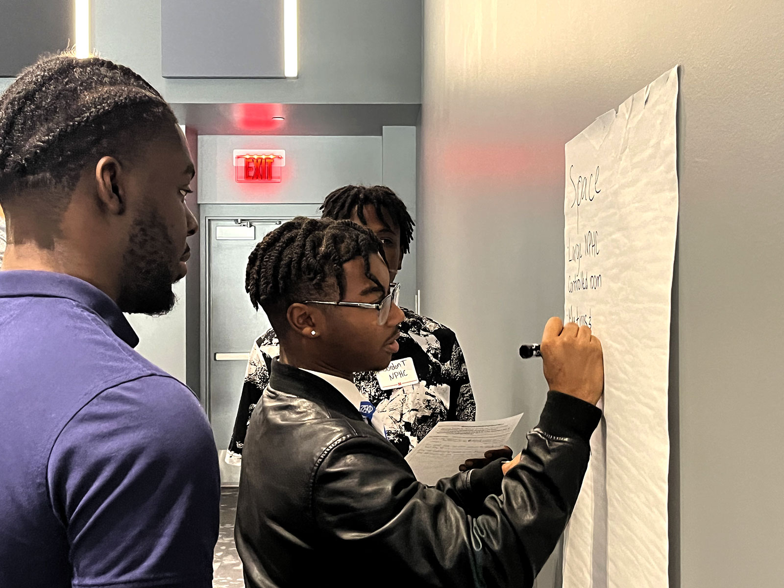 Two male students write on large post-it during meeting to offer feedback
