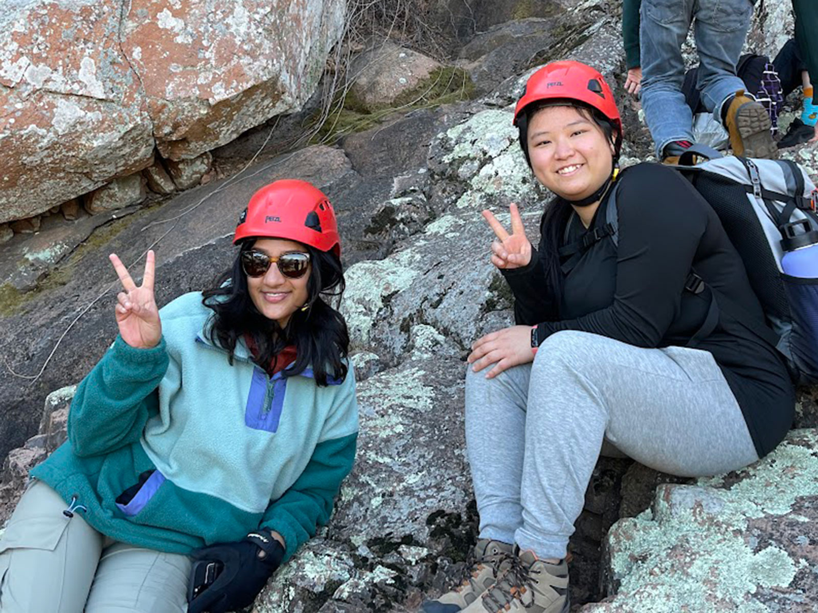 Two females climbing side of mountain pause while smiling for photo