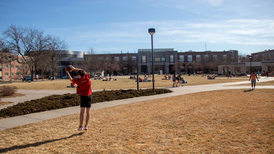 Students play catch with a football on the Meier Commons Green space.