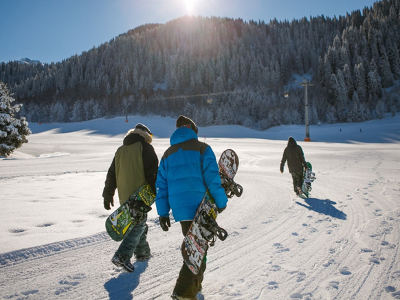Three people carry snowboards towards a ski lift.