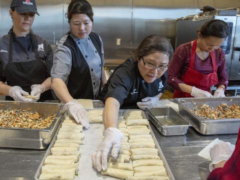 Thom “Emily” Tran (second from left) and Amy Tran (third from left) adjust raw egg rolls on a baking sheet in the Cather Dining Center on Jan. 9. For the second year, Cather Dining Center is offering handmade vegetarian egg rolls based on a recipe provided by Tran. The homemade option has proven popular with students and is healthier and cheaper than purchasing a frozen option.