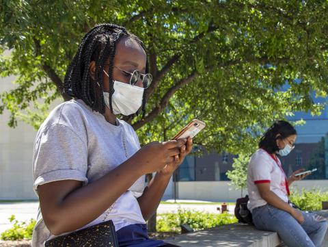 A black female student reads her smartphone outside the College of Education and Human Sciences building.