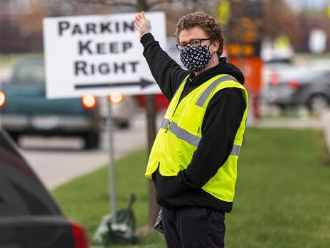 Noah Schwendeman directs traffic along Pinnacle Arena Drive as people arrive for their vaccine on April 7. Schwendeman said he volunteered for the clinic to help the community edge toward a return to normal. [ Craig Chandler | University Communication ]