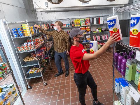 Morgan Berg (right), a senior in psychology from West Fargo, North Dakota, and Tim Anderson, a third-year law student from Huntington Beach, California, stock the shelves in the new East Campus Food Pantry. The pantry is in Filley Hall in the old Dairy Store walk-in freezer. [Craig Chandler | University Communication]