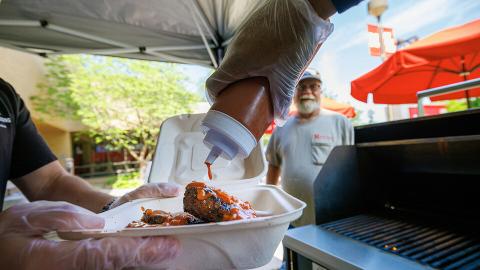Sean Jones, a line cook with Dining Services, adds Oklahoma BBQ sauce to Jeff Logans’ order of ribs and sausages.