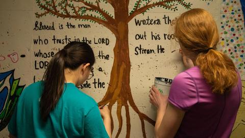 Ingrid Neuhaus (left) and Anna Youell (right) paint a mural depicting a bible quote in the tunnels connecting the Harper, Schramm and Smith residence halls on Thursday, March 21, 2024, in Lincoln, Nebraska.  [photo by Vivian Landis | Daily Nebraskan]