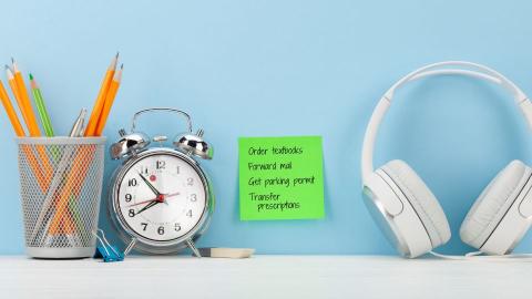 Pencil holder filled with pencils next to a clock, headphones, and a sticky note with a list of to-do items.