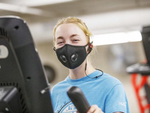 A student wears a black face covering while exercising in the Campus Rec Center's strength training & conditioning room.