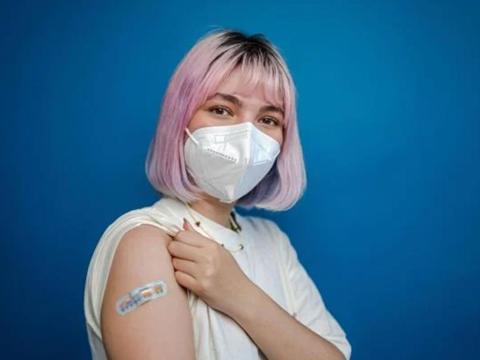 College-aged individual shows band aid from vaccination on arm