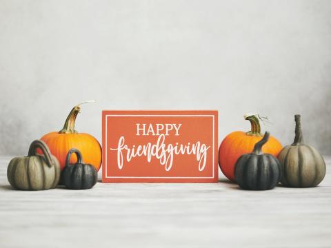 Sign with cursive text that reads "Happy Friendsgiving" surrounded by pumpkins