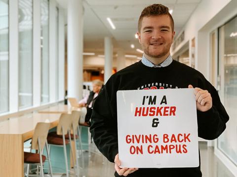 Troy Scheer holds sign with "I'm a Husker & Giving Back on Campus"