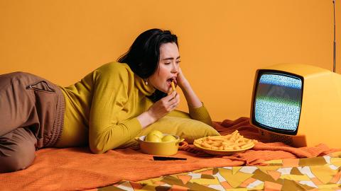 Woman in yellow long sleeve shirt watching TV and eating